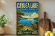 A vintage-style sign for Cayuga Lake State Park in New York, featuring a scenic image of the lake and surrounding landscape.