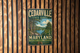 A vintage metal sign for the Cedarville State Forest in Maryland, featuring a scenic illustration of a forest and a lake.