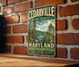A vintage-style metal sign for the Cedarville State Forest in Maryland, featuring a scenic illustration of a forest and a lake.