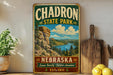 A vintage-style metal sign for Chardon State Park in Nebraska, featuring a scenic mountain landscape and a river.