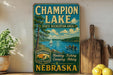 A vintage-style sign for Champion Lake, a state recreation area in Nebraska, featuring a scenic image of a lake with a sailboat and people enjoying various outdoor activities.