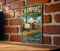 A vintage-style metal sign for the Champoeg State Heritage Area in Oregon, featuring an illustration of a wagon and a building.