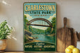 A vintage-style metal sign for Charlestown State Park in Indiana, featuring a scenic illustration of a bridge over a river surrounded by lush greenery.