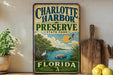 A vintage-style metal sign for Charlotte Harbor Preserve, Florida, featuring an illustration of a bird, palm tree, and water with a sun in the background.