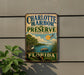 A vintage-style metal sign for Charlotte Harbor Preserve, Florida, featuring a scenic illustration of the park's natural surroundings.