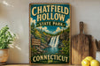 A vintage-style sign for Chatfield Hollow State Park in Connecticut, featuring a scenic illustration of a waterfall surrounded by lush greenery.