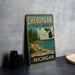 A vintage-style metal sign for Cheboygan State Park, featuring a scenic landscape with pine trees, a lake, and mountains.