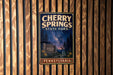 A vintage-style metal sign for Cherry Springs State Park in Pennsylvania, featuring a night sky scene with stars and a waterfall.