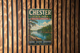 A vintage metal sign for Chester State Park in South Carolina, featuring a scenic landscape with a river and trees, mounted on a wooden wall.