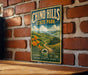 A vintage-style metal sign for Chino Hills State Park, featuring a scenic landscape with a winding path and orange flowers, mounted on a brick wall.