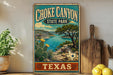 A vintage-style sign for Choke Canyon State Park in Texas, featuring a scenic landscape with a lake, mountains, and cacti.