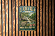 A vintage metal sign for Clark Creek Natural Area in Mississippi, featuring a waterfall and lush greenery.