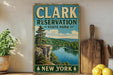 A vintage-style sign for Clark Reservation State Park in New York, featuring a scenic landscape with a lake and mountains.