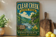 a vintage-style sign for Clear Creek State Park in Pennsylvania, with a scenic illustration of a river and forest.