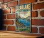 A vintage metal sign for Clear Lake State Park in California, featuring a scenic landscape with a lake, mountains, and a sailboat.