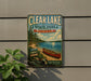 A vintage metal sign for Clear Lake State Park in Michigan, featuring a canoe on a lake surrounded by pine trees.