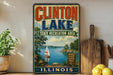 A vintage-style sign for Clinton Lake, Illinois, featuring a sailboat on the lake and a scenic landscape.