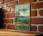 A vintage-style sign for the CockapSONSET State Forest in Connecticut, featuring a scenic landscape with a lake and pine trees.