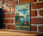 A vintage metal sign for Codorus State Park in Pennsylvania, featuring a scenic illustration of a lake, mountains, and a sailboat.