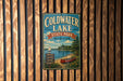 A vintage metal sign for Coldwater Lake State Park in Michigan, featuring a scenic illustration of a lake, a sailboat, and a forested shoreline.