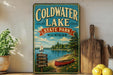 A vintage-style sign for Coldwater Lake State Park in Michigan, featuring a sailboat, a canoe, and a scenic landscape.