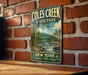 A vintage-style metal sign for Coles Creek State Park, featuring a scenic landscape with a river, trees, and mountains.