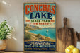 A vintage-style sign for Conchas Lake State Park in New Mexico, featuring a scenic image of the lake and mountains.