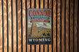 A vintage metal sign for the "Connor Battlefield State Historic Site" in Wyoming, featuring a monument and a horse-drawn carriage.