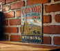 A vintage-style metal sign for the "Connor Battlefield State Historic Site" in Wyoming, featuring a monument and two figures in horseback riding.