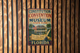 A metal sign for the Constitution Convention Museum in Florida, featuring an illustration of a historic building and a feather quill.