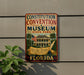 A vintage-style metal sign for the Constitution Convention Museum in Florida, featuring an American flag, a house, and a scroll with the text "We the People" and "Florida".