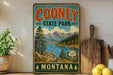 A vintage-style sign for Cooney State Park in Montana, featuring a scenic mountain landscape with a lake and pine trees.