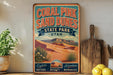 A vintage-style sign for Coral Pink Sand Dunes State Park in Utah, featuring a desert landscape with mountains and desert plants.