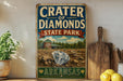 A vintage-style sign for Crater of Diamonds State Park in Arkansas, featuring an illustration of a diamond and a wooden sign with the text "Crater of Diamonds State Park Arkansas".