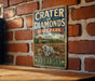 A vintage metal sign for Crater of Diamonds State Park in Arkansas, featuring a scenic image of the park and a large diamond.