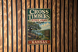 A vintage metal sign for Cross Timbers State Park in Kansas, featuring a scenic illustration of a river, trees, and mountains.