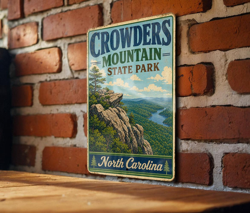 A vintage metal sign for Crowders Mountain State Park in North Carolina, featuring a scenic mountain landscape with a river and pine trees.