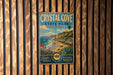 A vintage-style metal sign for Crystal Cove State Park, California, featuring a scenic beach landscape with palm trees and a house on the shore.