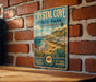A vintage-style metal sign for Crystal Cove State Park, California, featuring a scenic beach landscape with palm trees and a wooden house.