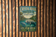 A vintage metal sign for Crystal River Preserve, featuring a manatee and surrounded by a tropical landscape, is displayed on a wooden wall.