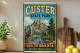 A vintage-style sign for Custer State Park in South Dakota, featuring a mountain landscape with a bighorn sheep in the foreground.