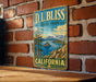 A vintage metal sign for D.L. Bliss State Park in California, featuring a scenic landscape with mountains, a lake, and a pine tree.