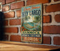 A vintage-style metal sign for Key Largo, Florida, featuring a hammock and palm trees, is displayed on a brick wall.