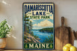 A vintage-style sign for Damariscotta Lake State Park in Maine, featuring a scenic landscape with a lake, mountains, and pine trees.