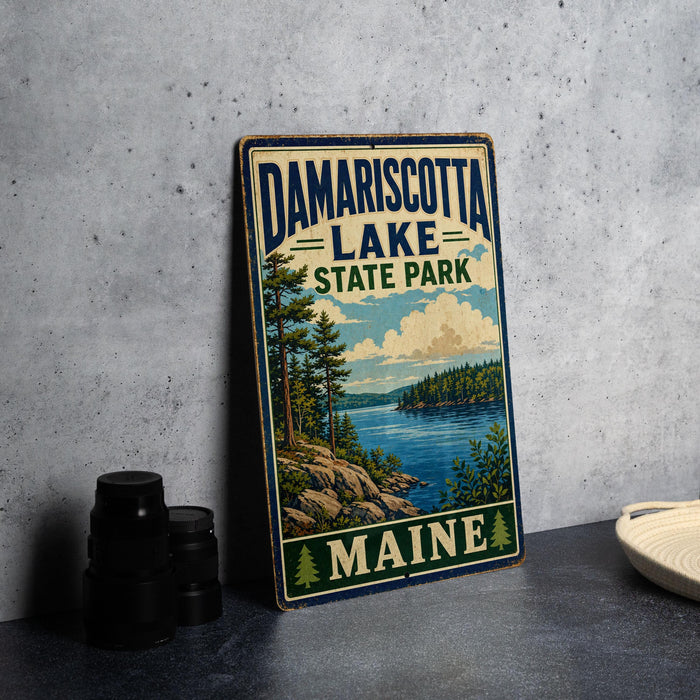 A vintage-style sign for Damariscotta Lake State Park in Maine, featuring a scenic landscape with a lake, mountains, and pine trees.