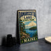 A vintage-style sign for Damariscotta Lake State Park in Maine, featuring a scenic landscape with a lake, mountains, and pine trees.