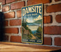 A vintage-style metal sign for Damsite State Park in New York, featuring a scenic landscape with a waterfall and a trail sign.