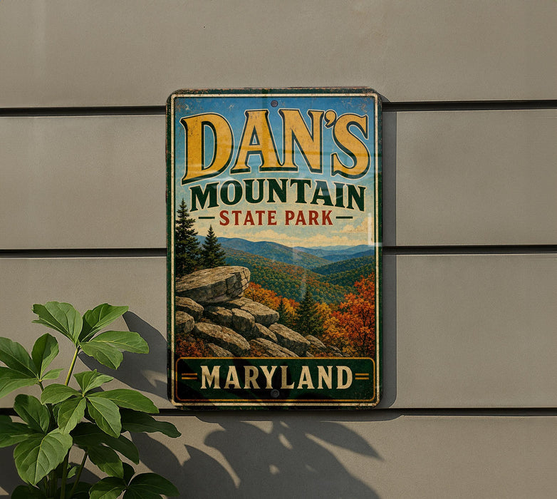 A vintage metal sign for Dan's Mountain State Park in Maryland, featuring a scenic mountain landscape with pine trees and rocky outcroppings.