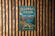 A vintage metal sign for Deadman's Basin State Park in Montana, featuring a scenic landscape with mountains, a lake, and a buffalo.
