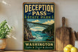 A vintage-style metal sign for Deception Pass State Park in Washington, featuring a scenic illustration of a bridge over a river surrounded by mountains and pine trees.